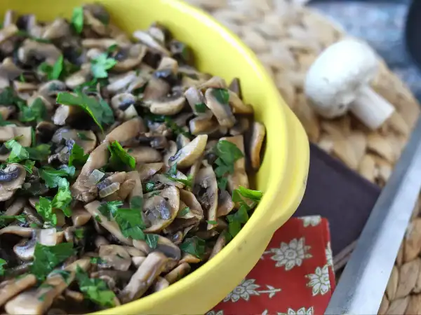 Un piatto giallo pieno di saporiti funghi in padella, guarniti con prezzemolo fresco.