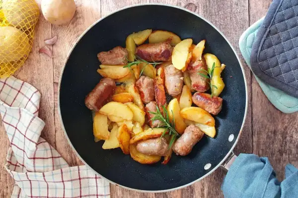 Salsiccia e patate in padella, dorate e profumate, con rametti di rosmarino. Un piatto rustico e invitante.