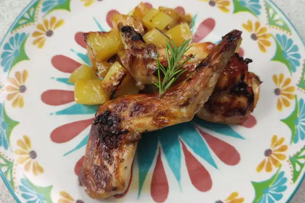 Roasted rabbit pieces with golden potatoes and a rosemary sprig on a colorful floral plate.