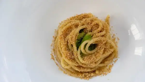 Un piatto di pasta alla carrettiera, spaghetti conditi con mollica tostata e verdure verdi, serviti su un piatto bianco.