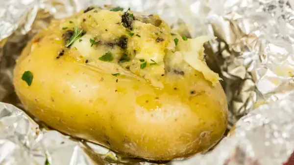 Patate ripiene al forno, dorate e fumanti, avvolte in carta stagnola, con un ripieno cremoso e erbe aromatiche.