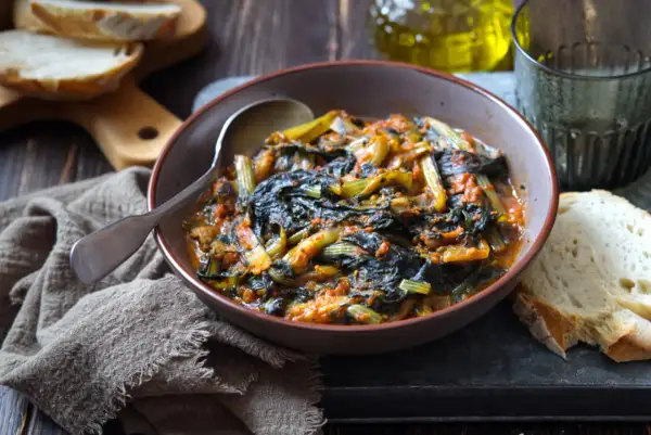 Cicoria in padella, un piatto rustico e saporito, servito in una ciotola con pane fresco e un bicchiere d'acqua.