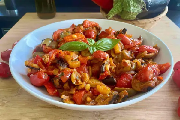 Caponata ricetta semplice: un piatto colorato con melanzane, peperoni, pomodorini e basilico fresco.