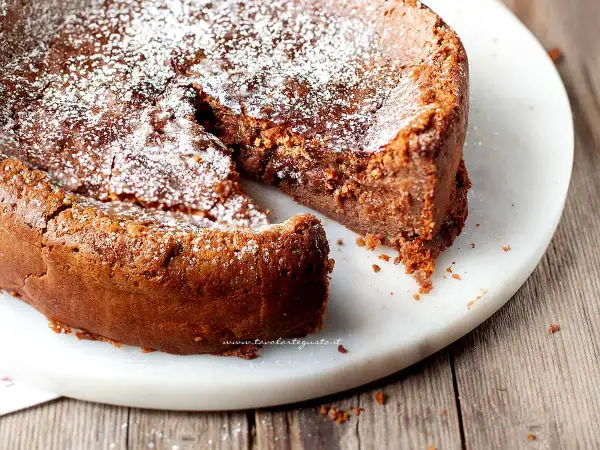 Una deliziosa torta al cioccolato al latte, cosparsa di zucchero a velo, con una fetta mancante che invita ad assaggiarla.